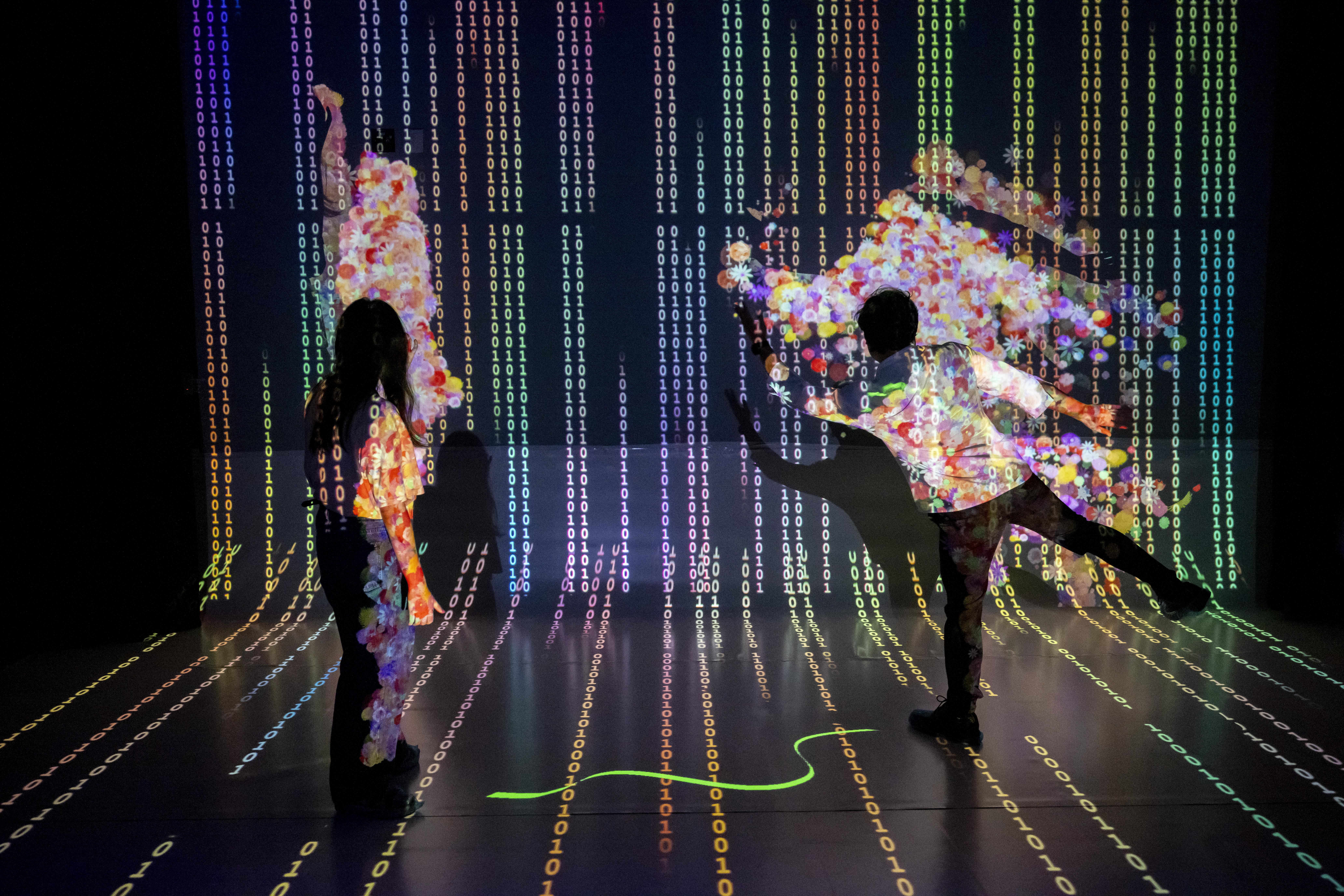 Two people interacting with an immersive projection piece on the wall and floor with pastel colors